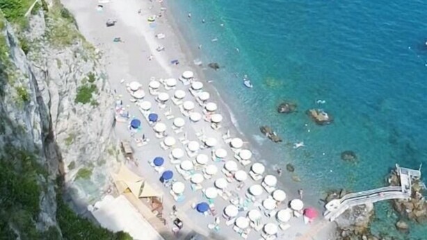 Une plage côtière bordée d’une eau d’un bleu limpide, d’une falaise rocheuse et d’une rangée de parasols de plage.