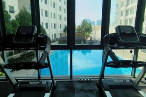 Une salle de sport équipée de tapis de course et dotée d’une grande fenêtre donnant sur une piscine.