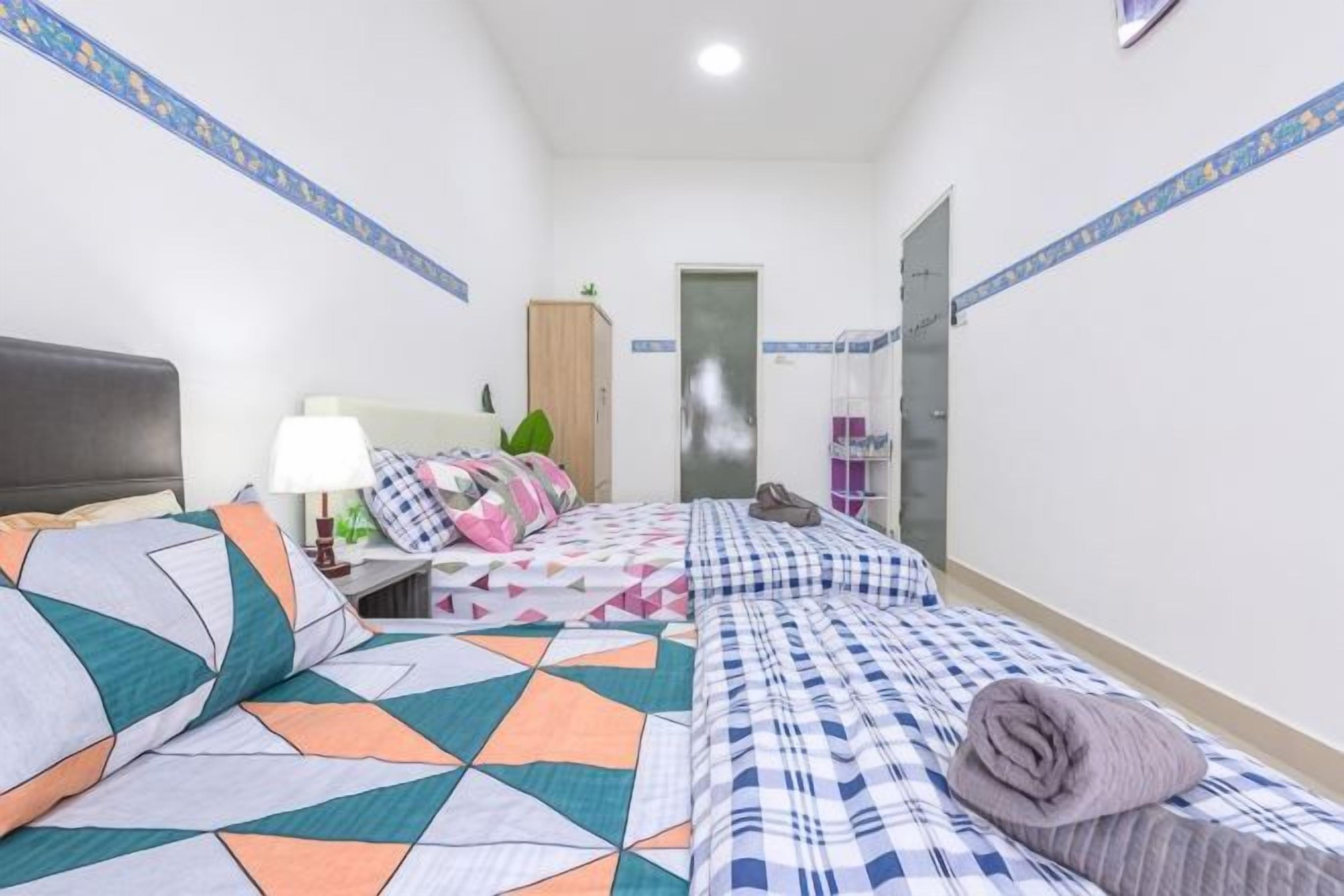 A hotel room with two beds, a nightstand, a lamp, a wardrobe, and a door leading to a bathroom.