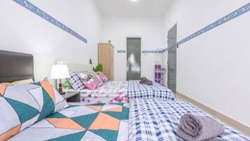 A hotel room with two beds, a nightstand, a lamp, a wardrobe, and a door leading to a bathroom.