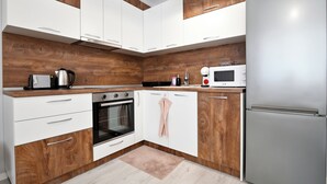 Een moderne keuken met witte kasten, een houten accentmuur, een roestvrijstalen koelkast en een magnetron.