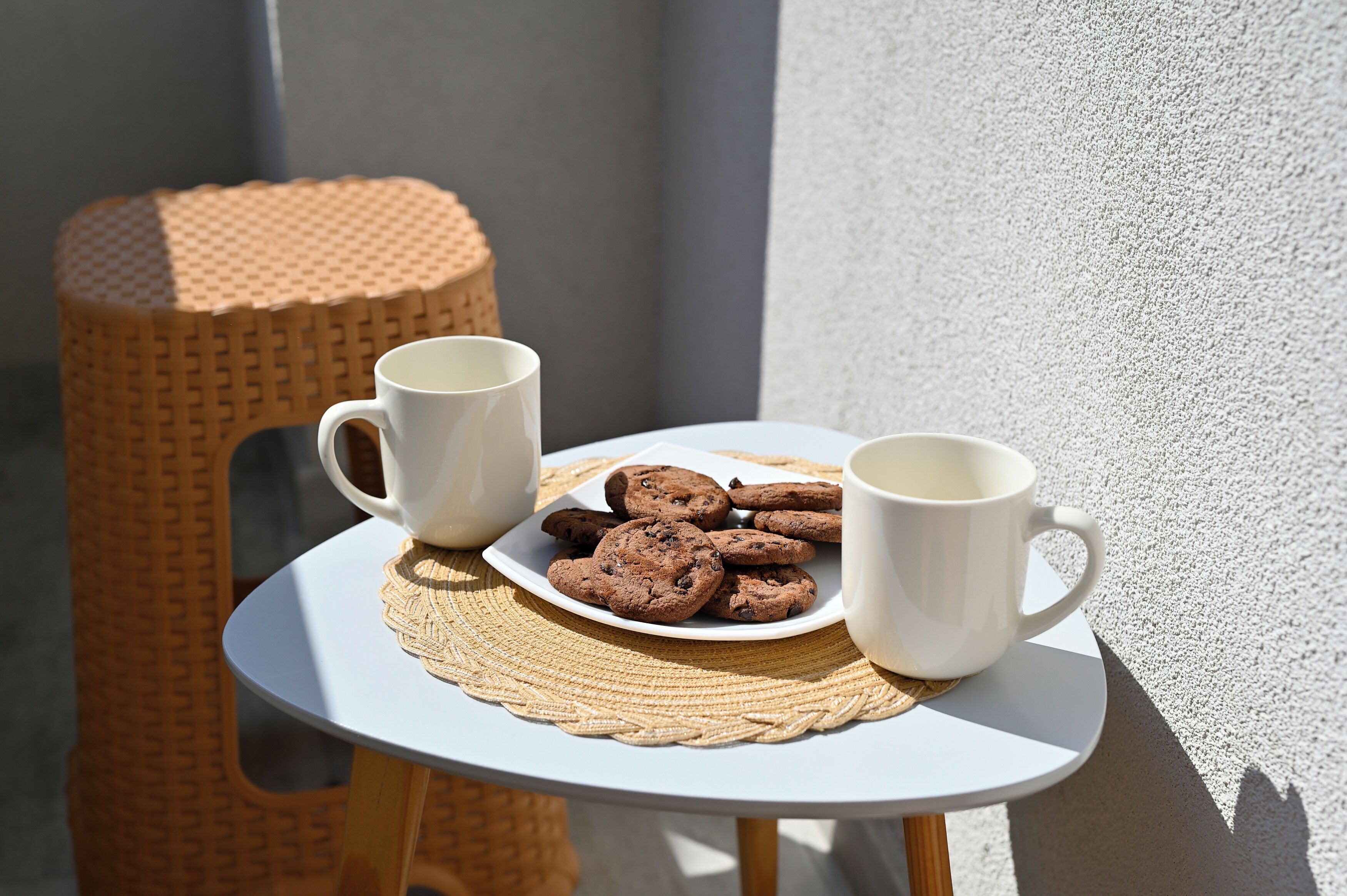 A small round table with a white plate of cookies and two white mugs.