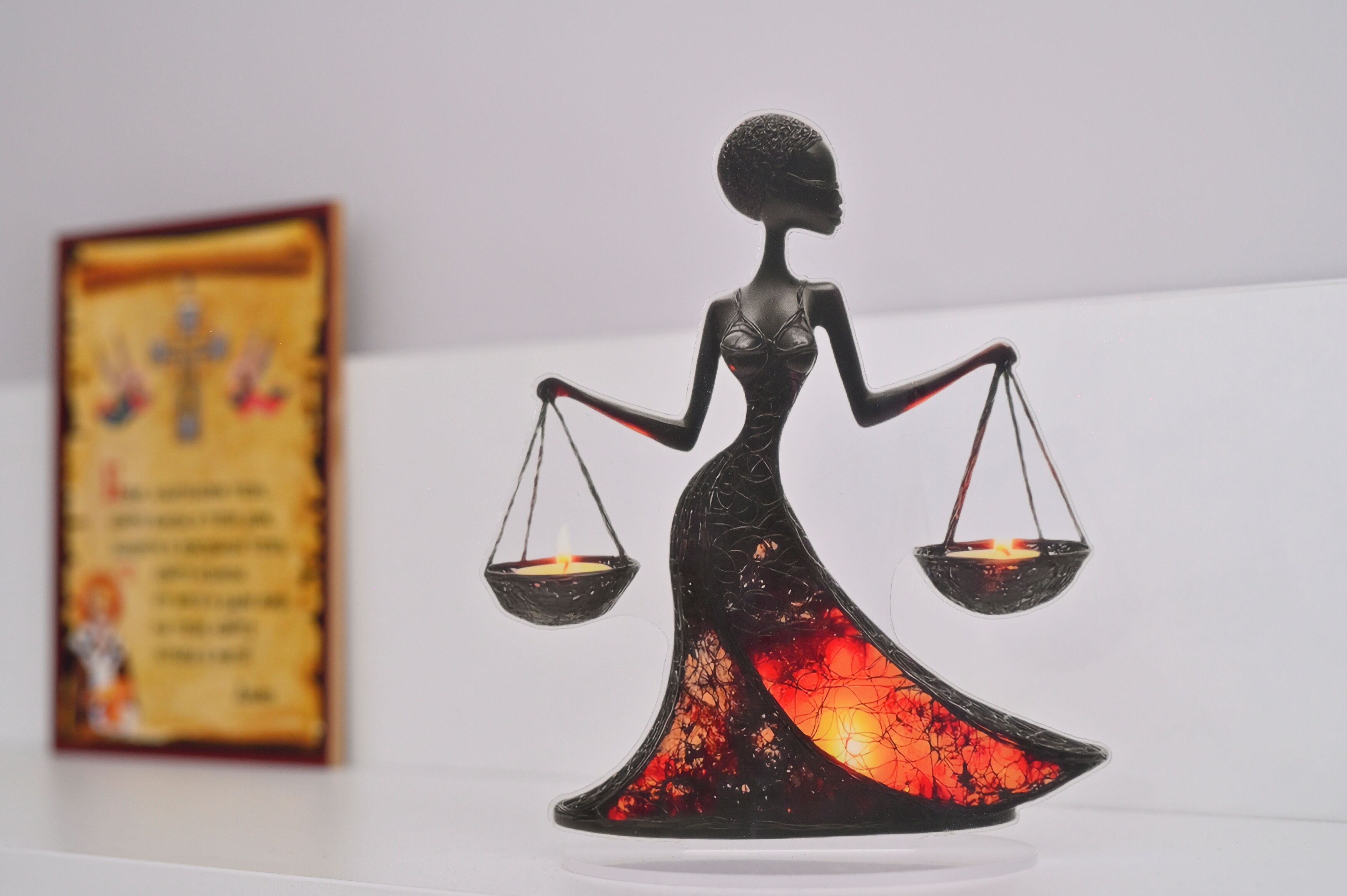 Une statue représentant une femme tenant une balance, avec une bougie allumée dans chaque plateau.