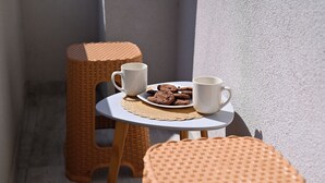 Een klein terras met rieten krukjes en een tafel, een bord met koekjes en twee witte bekers.