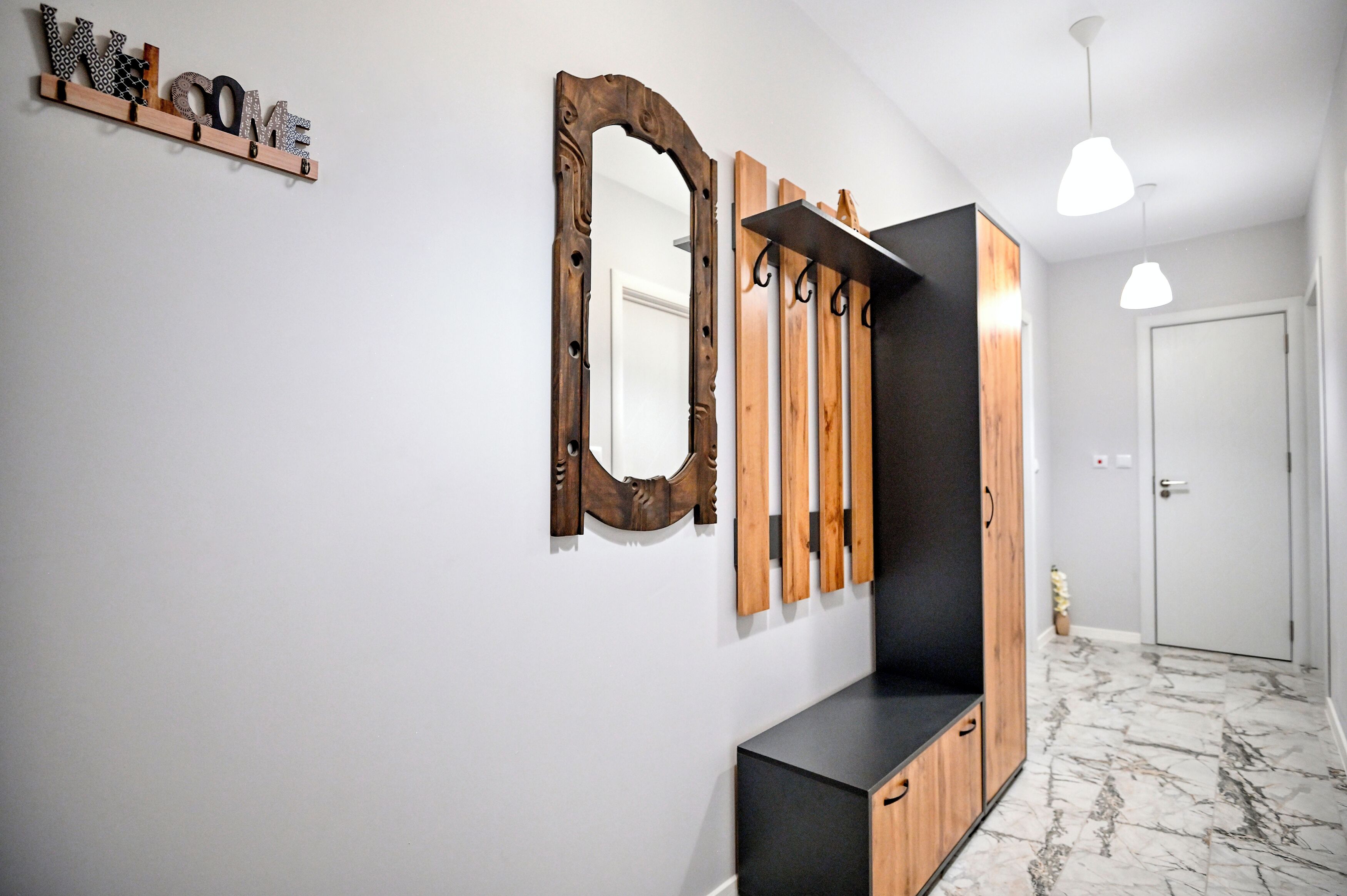 A hallway with a 'WELCOME' sign, a mirror, and a wooden shelf.