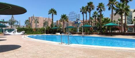 A swimming pool with a tiled deck, surrounded by palm trees and a clear sky.