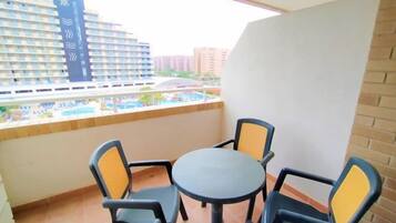 Un balcón con mesa y sillas, con vistas a una piscina y edificios.