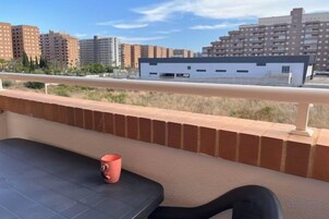 Un balcón con un muro de ladrillo, una mesa y una taza roja.