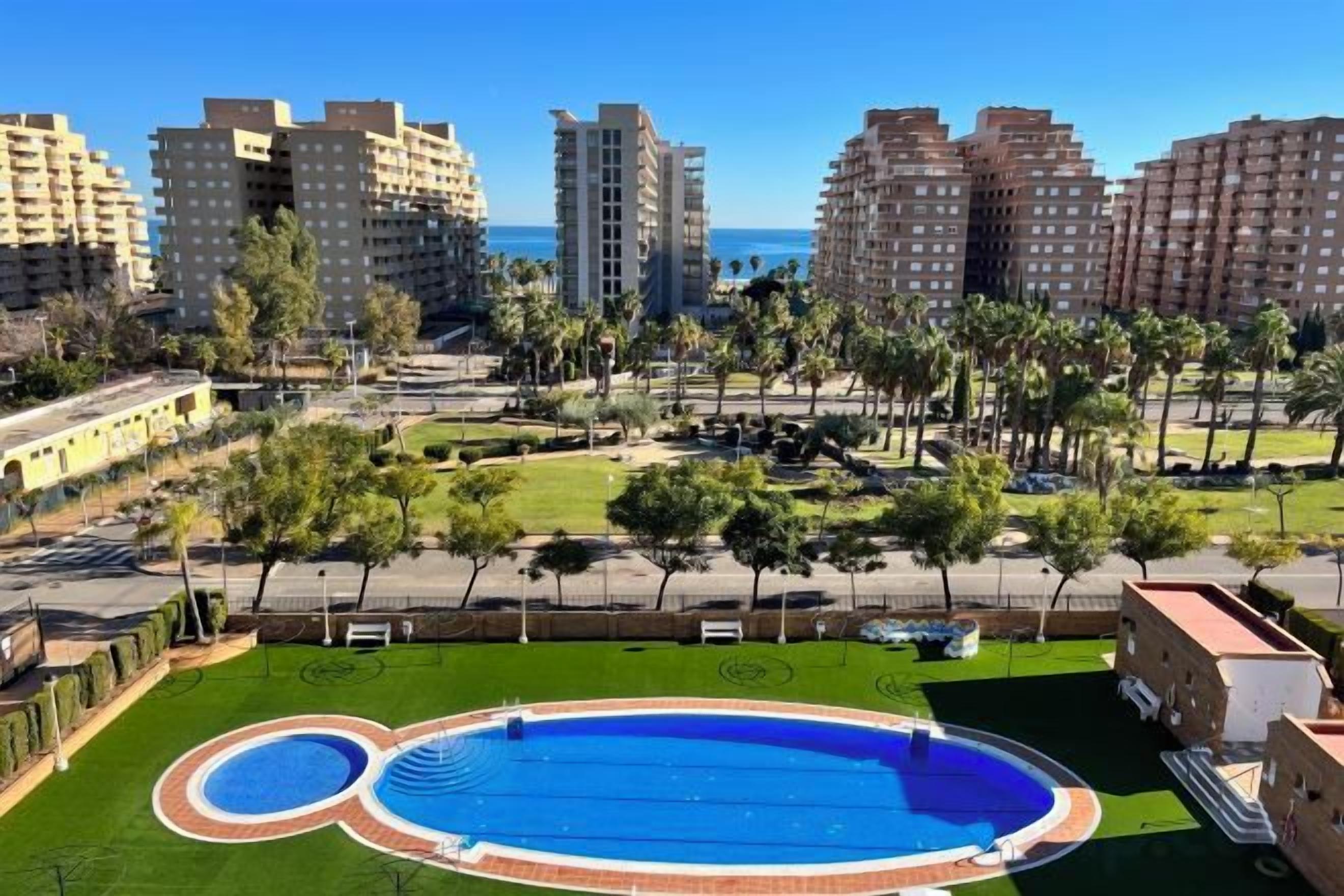 Zona residencial con piscina, césped verde y edificios altos al fondo.