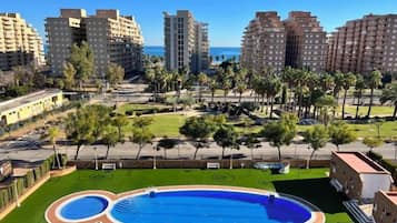 Zona residencial con piscina, césped verde y edificios altos al fondo.