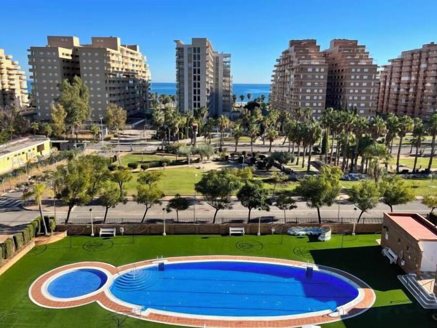 A residential area with a swimming pool, green lawns, and tall buildings in the background.