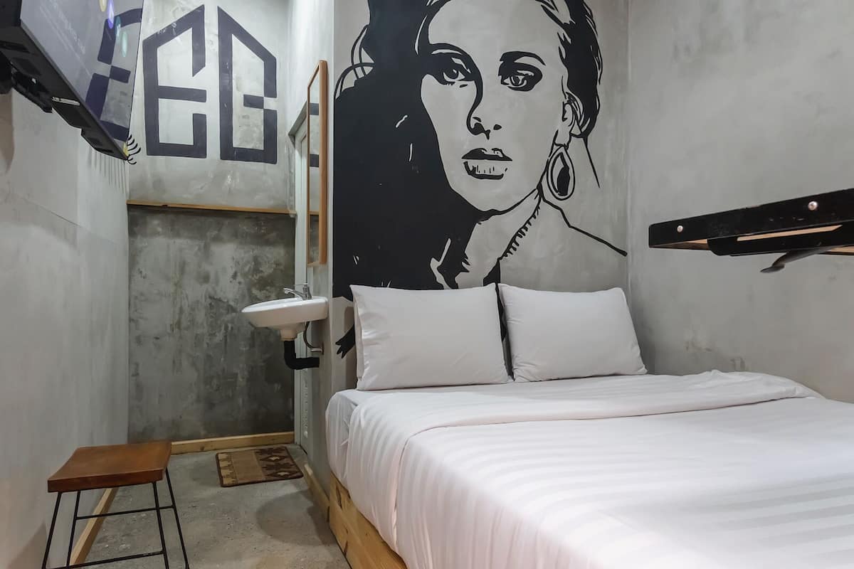 A small, modern bedroom with a bed, a bedside table, a wall-mounted shelf, and a large abstract painting.
