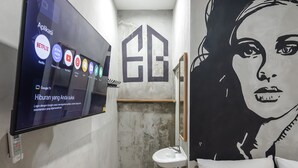 A bathroom with a large mirror, a sink, and a toilet. There is a TV mounted on the wall displaying various streaming services. - Exotic Inn Semarang, by INNCA COLLECTION (Semarang)