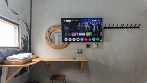 A hotel room with a TV mounted on the wall displaying various streaming services, a wooden desk with a chair, a bed, and a small trash bin. - Exotic Inn Semarang, by INNCA COLLECTION (Semarang)