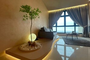 A modern living room with a large window, a sofa, a small table, and a decorative tree. - L23-ParadigmMall Residence Skudai JB 3R2B-10pax (Tebrau)