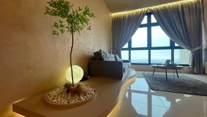 A modern living room with a large window, a sofa, a coffee table, and a decorative plant. - L23-ParadigmMall Residence Skudai JB 3R2B-10pax (Tebrau)