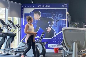 A gym with treadmills, a stationary bike, and a large poster on the wall. - Cozy Homestay 2 BR sea view 29th flr Halong center. (Ha Long)