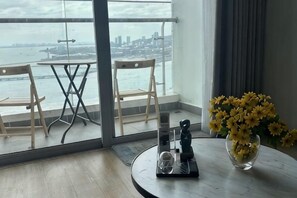 A room with a view of the city skyline through large windows, a round table with a vase of flowers, and two wooden chairs. - Cozy Homestay 2 BR sea view 29th flr Halong center. (Ha Long)