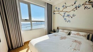 Une chambre avec un grand lit, une fenêtre avec des rideaux et un mur orné d’une fresque florale.