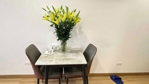 A dining table with two chairs, a vase with yellow flowers, and a pair of slippers on the floor. - Era Apartment Trung Liet (Hanoi)