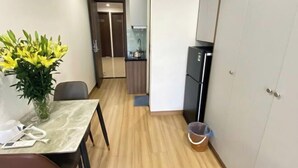 A compact kitchen with a refrigerator, a dining table with chairs, a vase of flowers, and a trash bin. - Era Apartment Trung Liet (Hanoi)