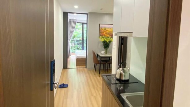 A compact kitchen with a sink, stove, and a dining area visible in the background. - Era Apartment Trung Liet (Hanoi)