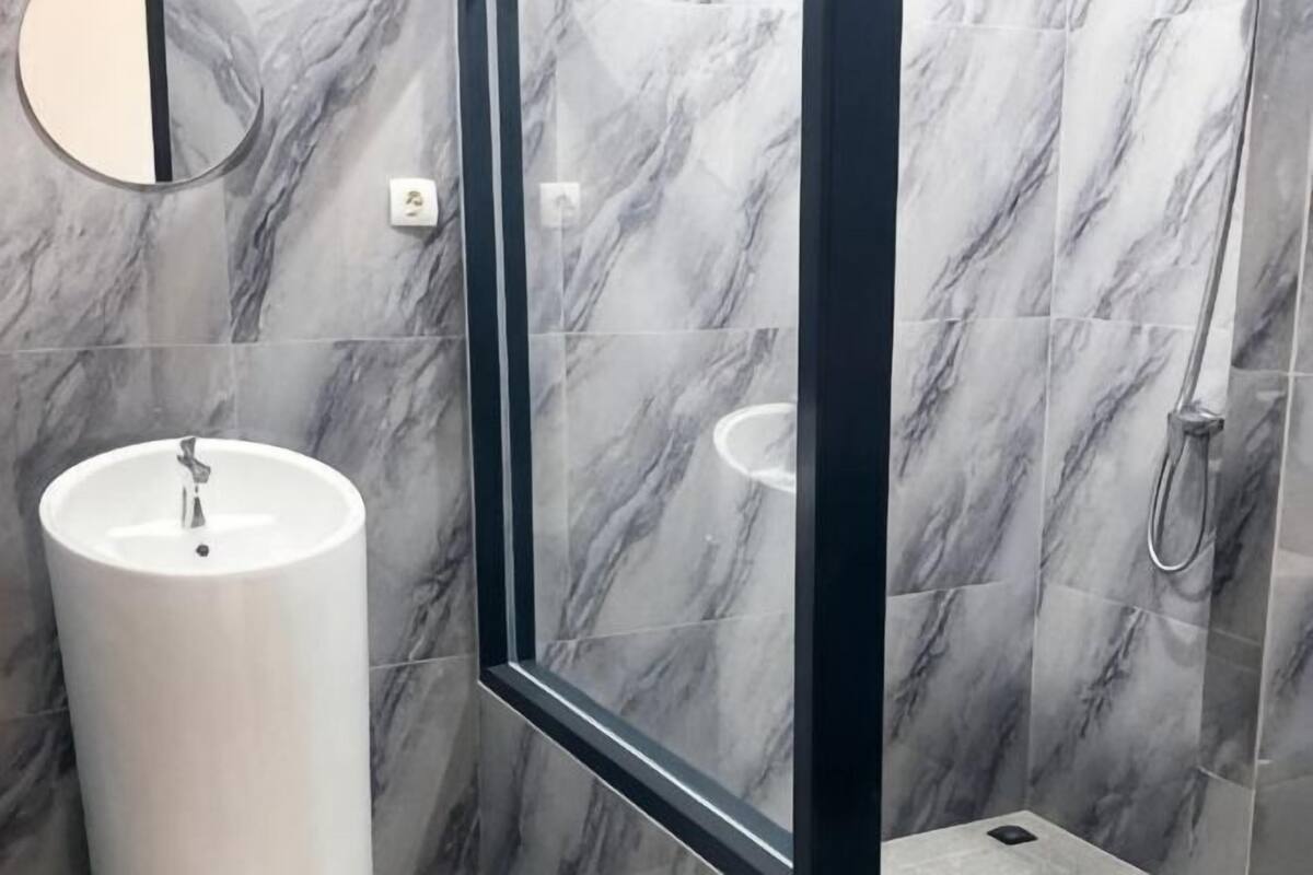 Un baño con piso de mármol, un lavamanos blanco, un espejo y zona de ducha.