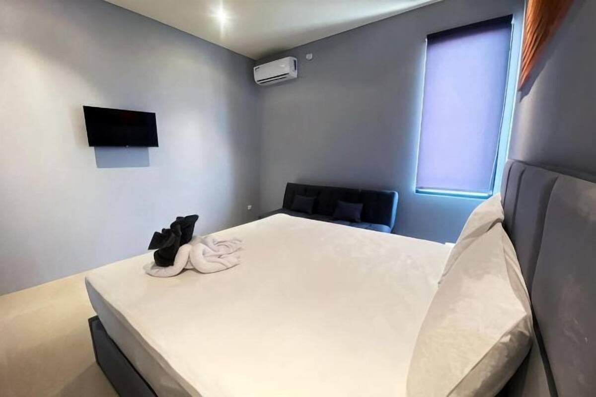 Un dormitorio moderno con una cama grande, un televisor de pantalla plana en la pared y una ventana con persianas.