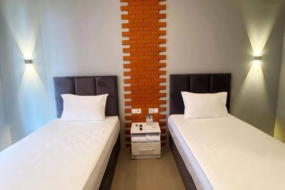 Habitación de hotel con dos camas, una pared decorada con ladrillos e iluminación en la pared.