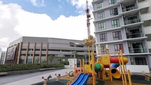 Een speeltuin met glijbanen en klimconstructies, een gebouw met meerdere verdiepingen en balkons, en een heldere lucht.