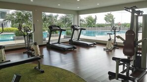 Een sportschool met loopbanden, een bank en trainingsapparatuur, met uitzicht op een zwembad.