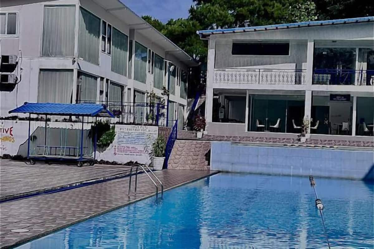 Une piscine située à côté d’un bâtiment doté de nombreuses fenêtres et d’un espace abrité.