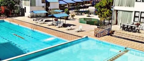 A swimming pool with lounge chairs and umbrellas, surrounded by buildings and trees.