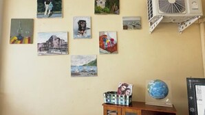 A wall with various artworks, a GREE air conditioning unit, and a wooden cabinet with drawers. - Eco hostel Bangsaen (Chon Buri)