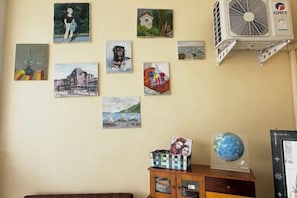 A wall with various artworks, a GREE air conditioning unit, and a wooden cabinet with drawers. - Eco hostel Bangsaen (Chon Buri)
