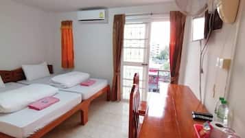 A hotel room with two beds, a wooden table, a fan, and a view of the outside.