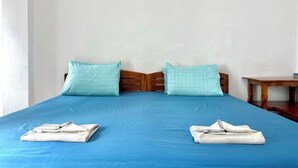 A bed with a blue mattress and two pillows, a wooden headboard, and a small wooden table beside the bed. - Eco hostel Bangsaen (Chon Buri)