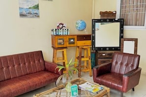 Ein Wohnzimmer mit einem roten Sofa, einem Ledersessel, einem Couchtisch mit Zeitschriften, einer kleinen Pflanze und einer Holzkabine mit Schubladen.