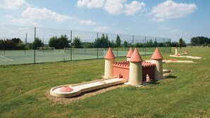A castle-themed playground with a tennis court in the background. - Camping Domaine de la Brèche (Varennes sur Loire)
