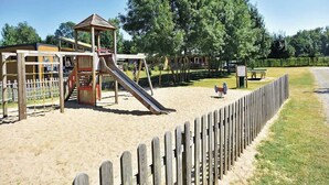 A playground with a slide and climbing structures, surrounded by a wooden fence and trees. - Camping Domaine de la Brèche (Varennes sur Loire)