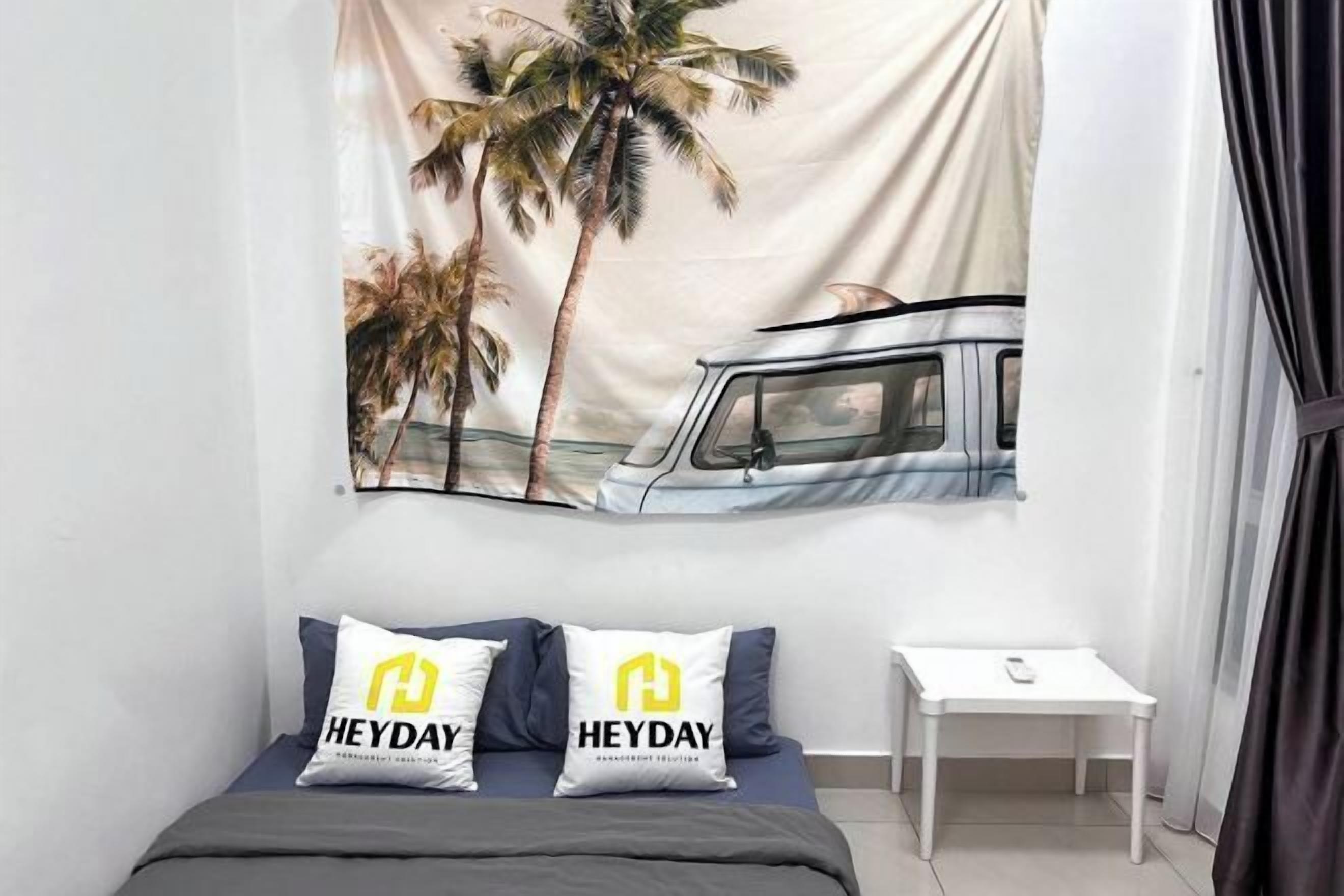 A bedroom with a bed, two pillows with 'HEYDAY' branding, a small white nightstand, and a tapestry with a car and palm trees.