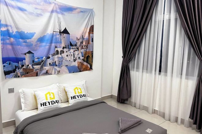 A hotel room with a bed, a tapestry depicting a coastal town, and a window with sheer curtains.