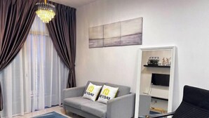 A modern living room with a grey sofa, a black chair, a blue rug, and a chandelier.