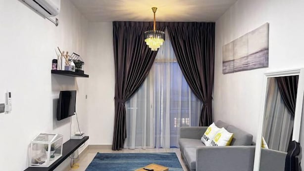 A modern living room with a grey sofa, a wooden coffee table, a mounted TV, and a chandelier.