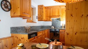 Une cuisine avec des meubles de rangement en bois, un plan de travail en granit, une cuisinière et une horloge au mur.