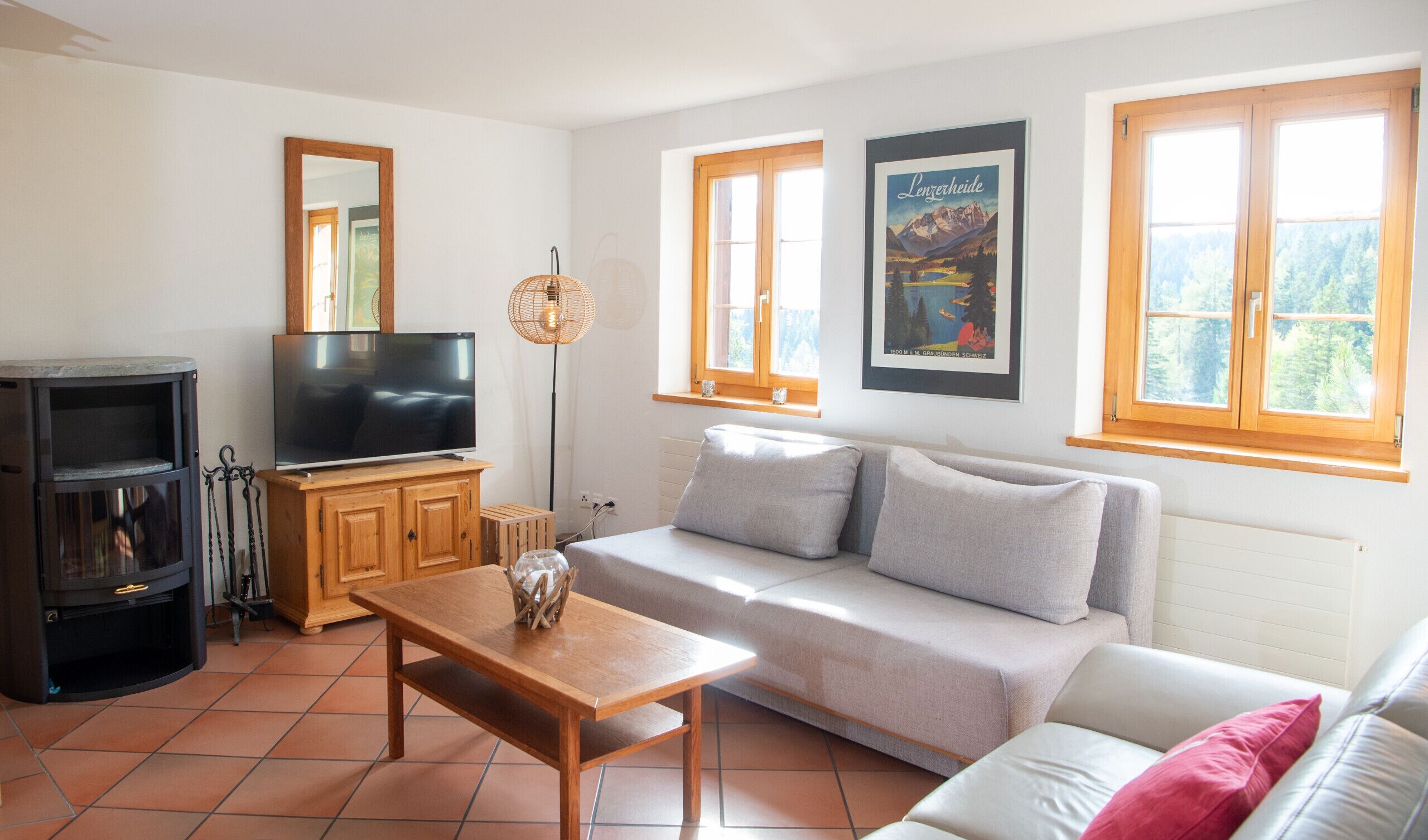 Un salon avec un canapé, un téléviseur, un meuble en bois et une fenêtre ornée d’une affiche.