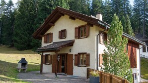 Une maison de style chalet, avec un toit en pente, des volets en bois et une cheminée en pierre.