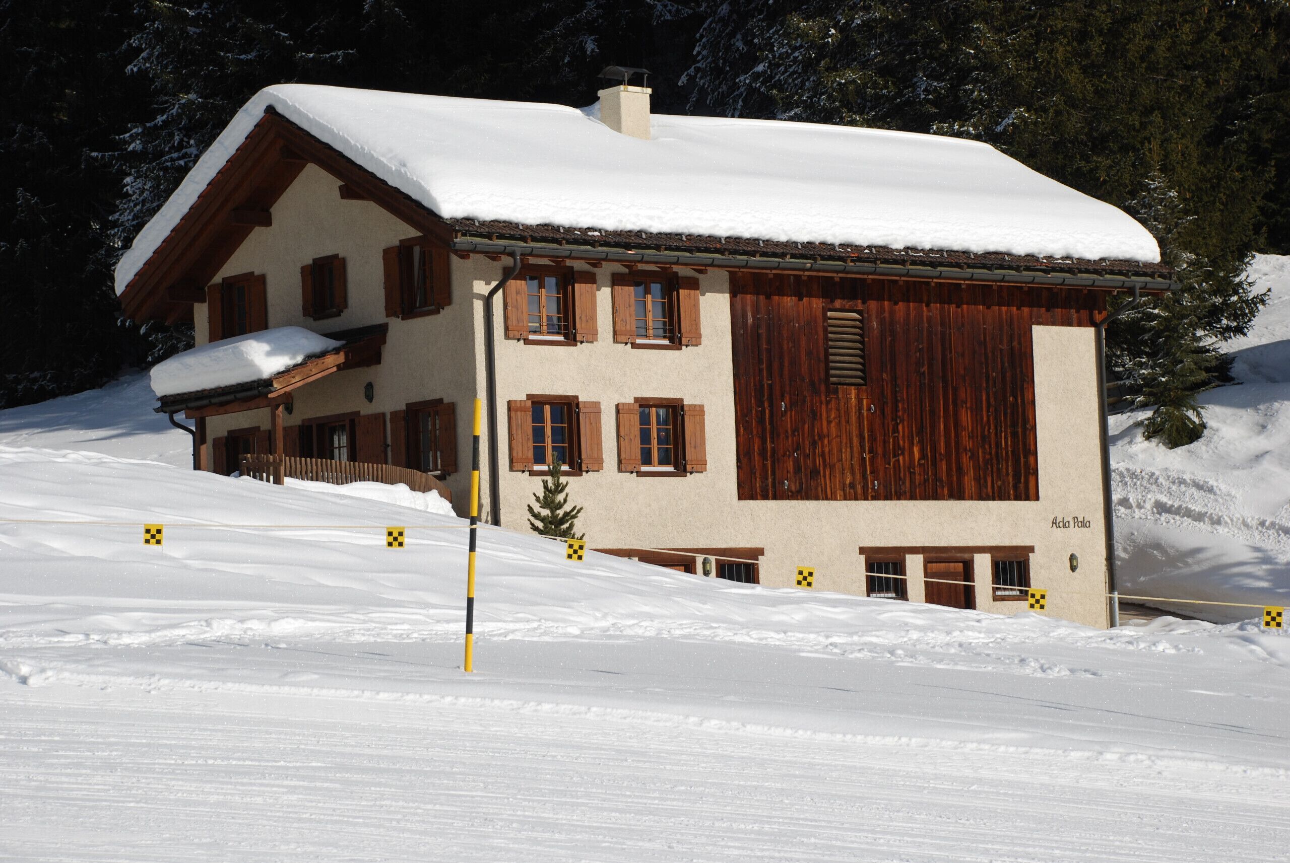 Ein Chalet mit schneebedecktem Dach, Holzläden und einem Schornstein.