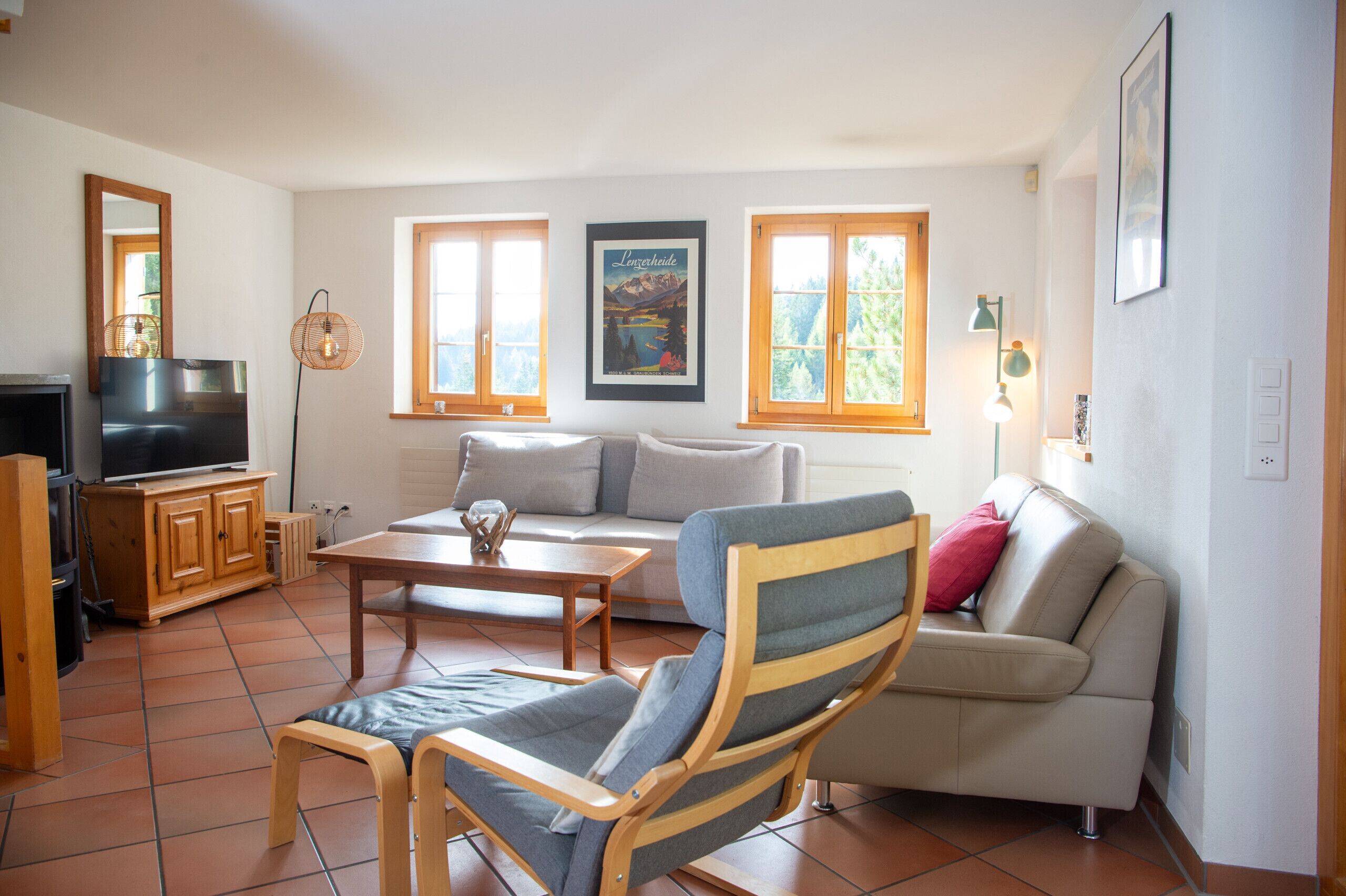 Ein Wohnzimmer mit Sofa, Sessel, Couchtisch, Fernseher und Holzschrank.