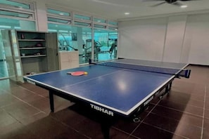 Une table de ping-pong avec une raquette, située dans une pièce équipée de matériel de sport et dotée d’un mur en verre.